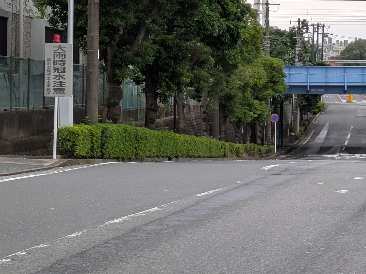 鉄道の下へ下る道の脇に「大雨時冠水注意」の看板が立っている